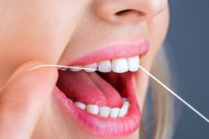 Cierre de una persona que usa hilo dental entre dientes, destacando las prácticas de higiene oral relacionadas con el mantenimiento de la salud dental mientras usa medicamentos para la pérdida de peso.